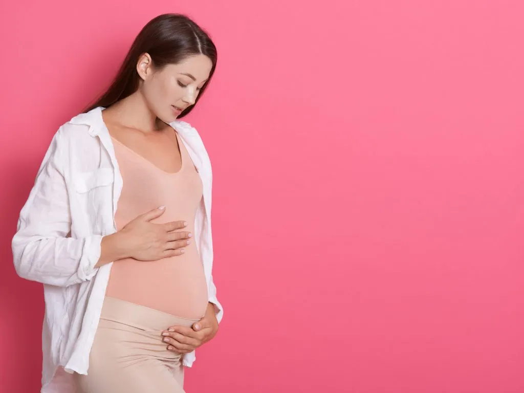 Beautiful pregnant woman hugging her tummy against pink background, looking at her belly with love, copy space for advertisement or promotional text text. Beautiful pregnant woman hugging her tummy against pink background, looking at her belly with love, copy space for advertisement or promotional text text.